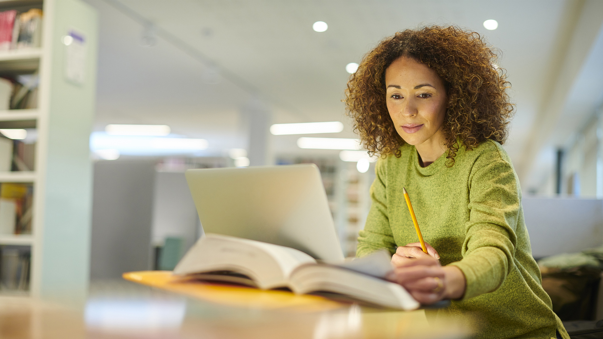 woman writes on paper with an open laptop in front of her while sitting in a library