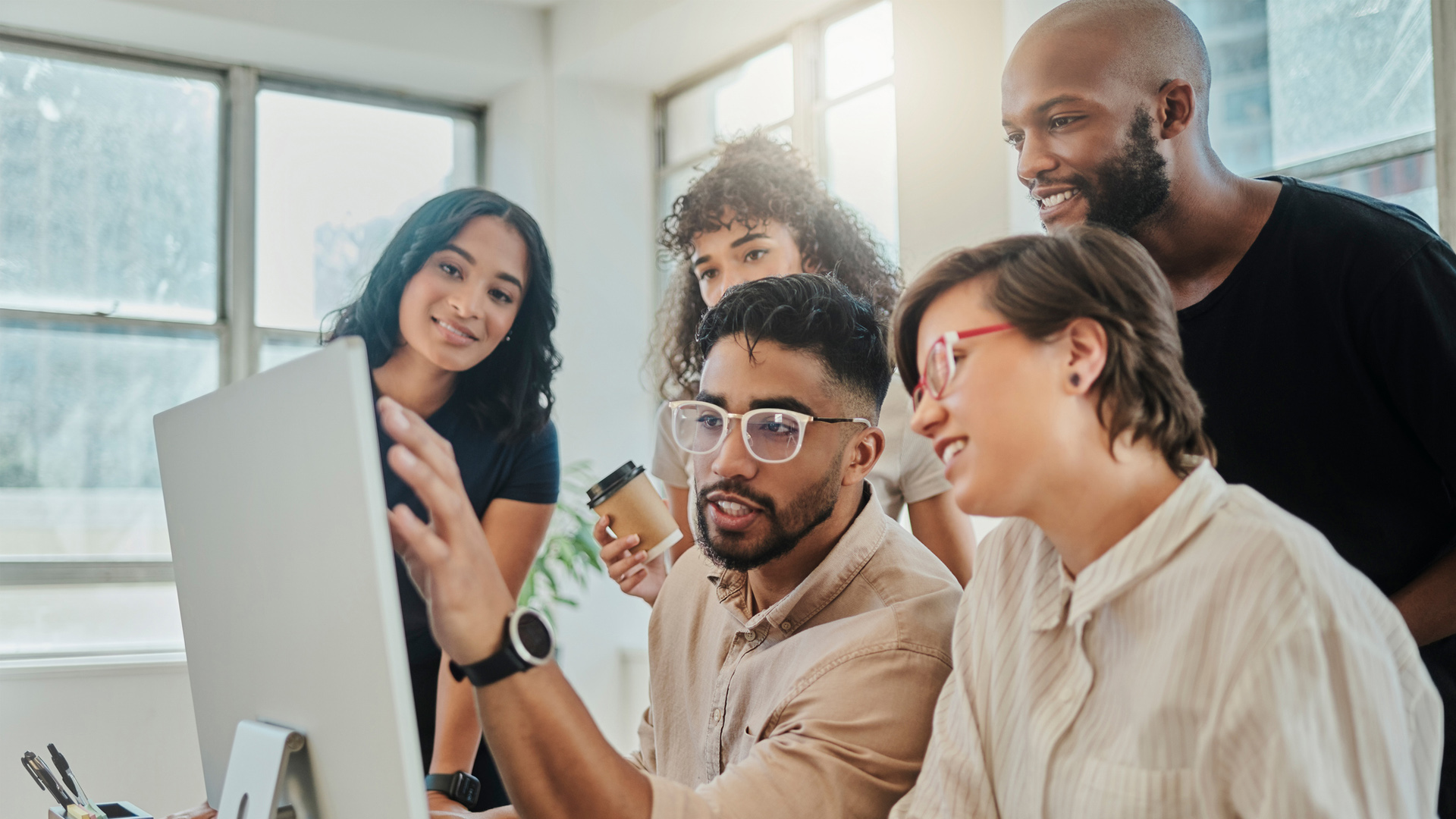 a team gathered around a computer monitor while a person in a lead role explains