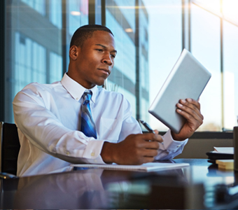 Professional man holding a tablet sitting at a desk and writing on a notebook
