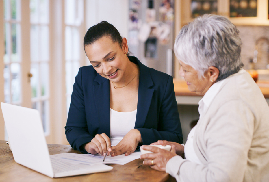 woman at laptop computer shows an older woman something on a peice of paper