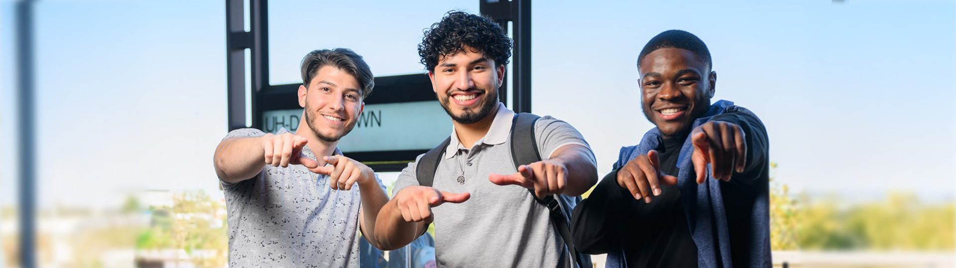Three male students pointing in the direction of the viewer