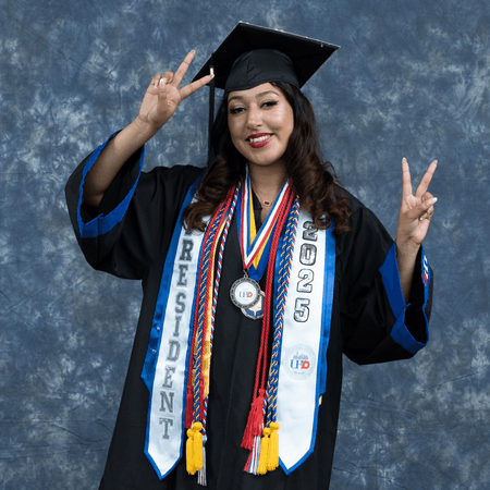 Emily Martinez gives two peace signs while wears graduation cords, a stole, cap and gown at the University of Houston Downtown's 78th Commencement Ceremony 