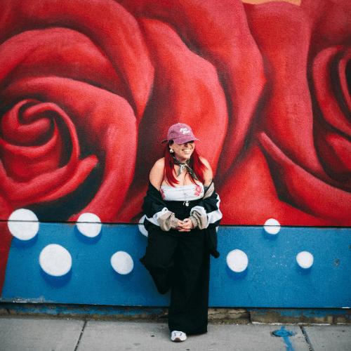 Magge Nunez a University of Houston-Downtown alumna smiles with a mural of a rose behind them. Nunez is a DJ in Houston, Texas.