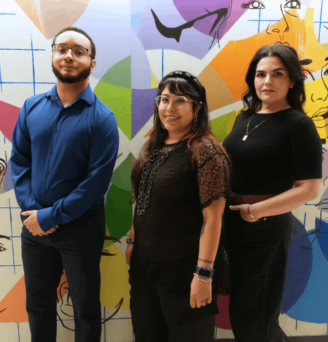 Kettani Zeroual, Ophelia Palomo, and Becky Ditto smile in front of a student created mural at the university of houston-downtown. The three students are in the University of Houston-Downtown's Chapter of Psi Chi. 