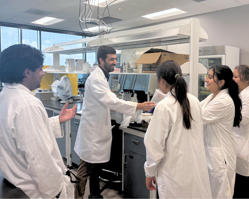 Four students in lab coats interact with a professor at the university of houston-downtown.