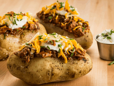 Three baked potatoes loaded with sour cream, cheese, bacon bits, and shredded meat.
