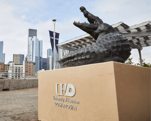 an alligator statue on the university of houston-downtown's south deck. the downtown houston skyline is in the background.